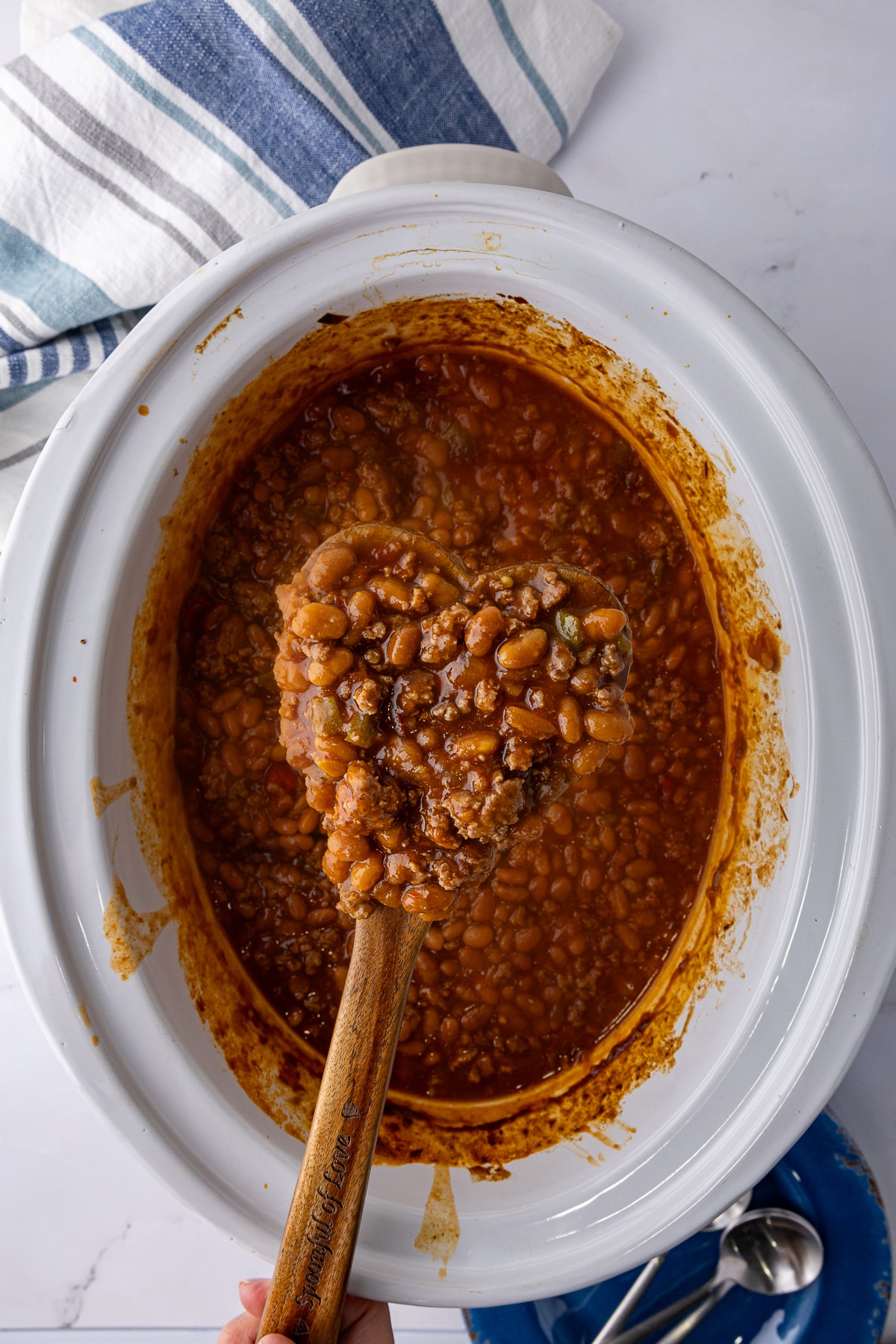 heart shaped wooden spoon with baked beans and hamburger over a crock pot of southwest baked beans