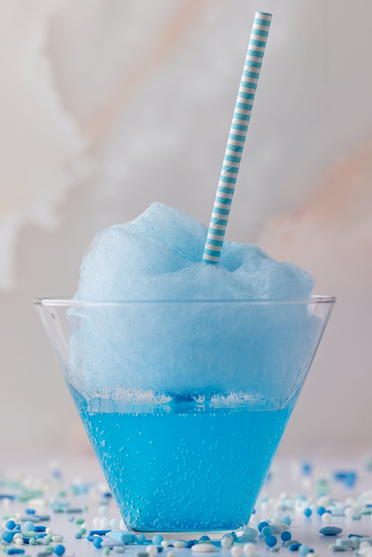single blue soda in a v shaped glass with cotton candy suspended and a blue and white striped straw
