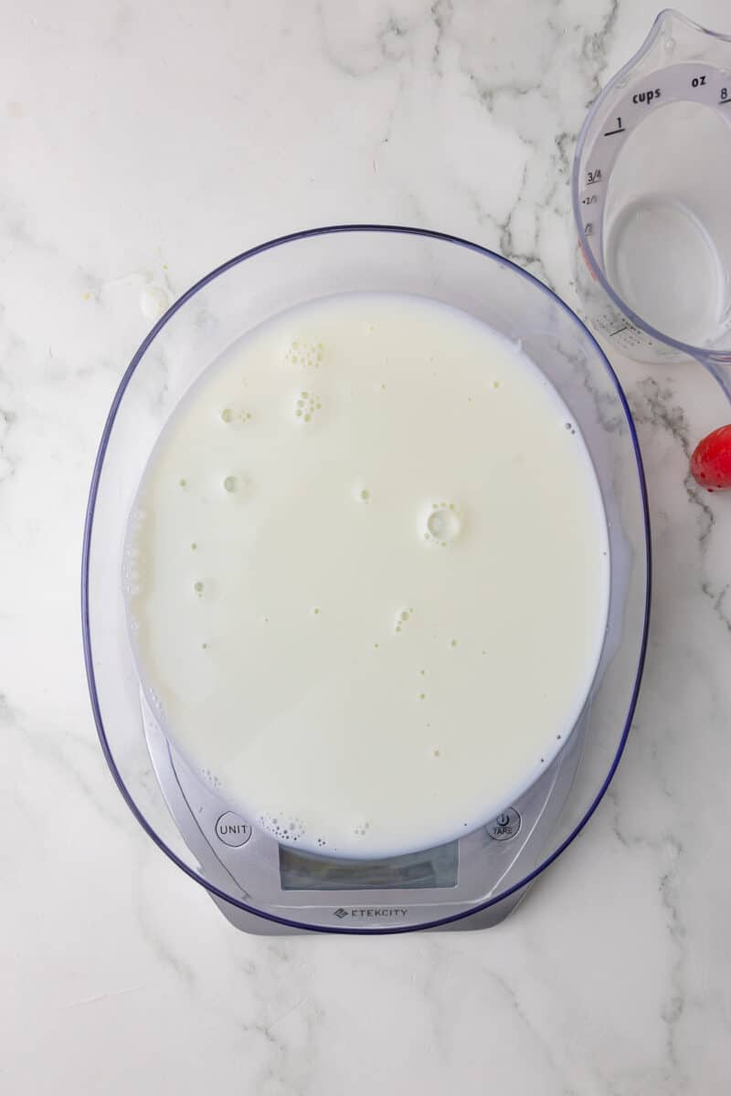 milk being measured on a scale with a wet measuring cup in the background on a white countertop