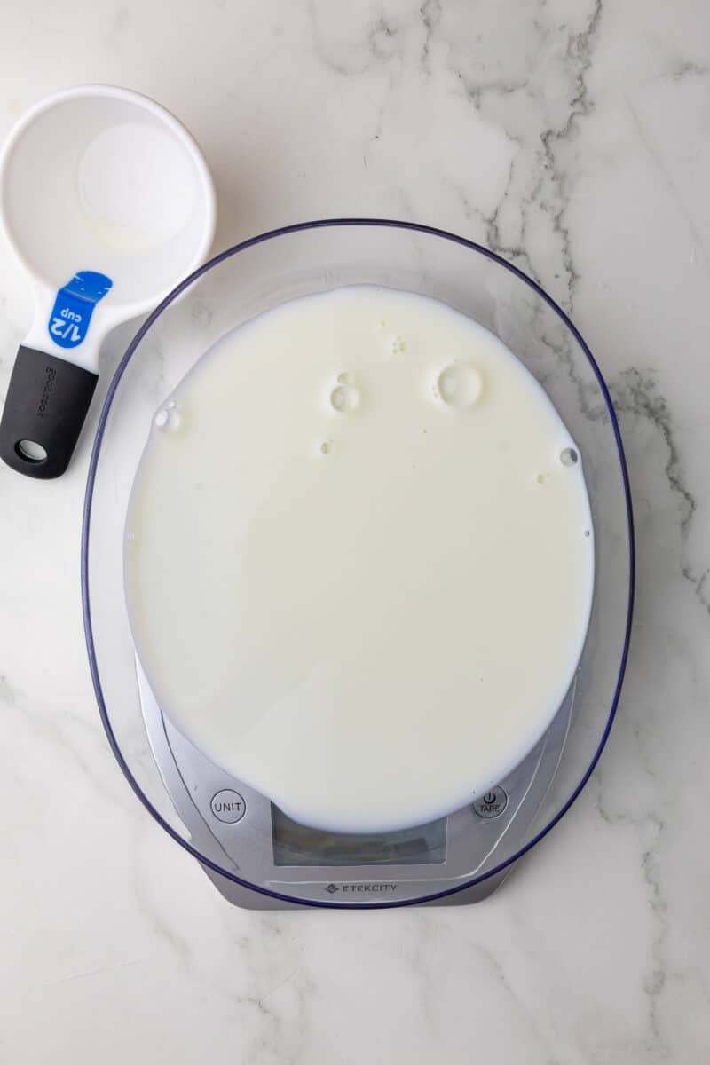 milk being measured on a scale with a dry measuring cup in the background on a white countertop