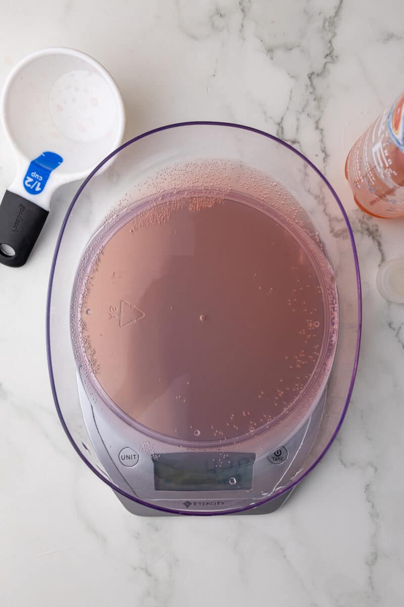 soda being measured on a scale with a dry measuring cup in the background on a white countertop