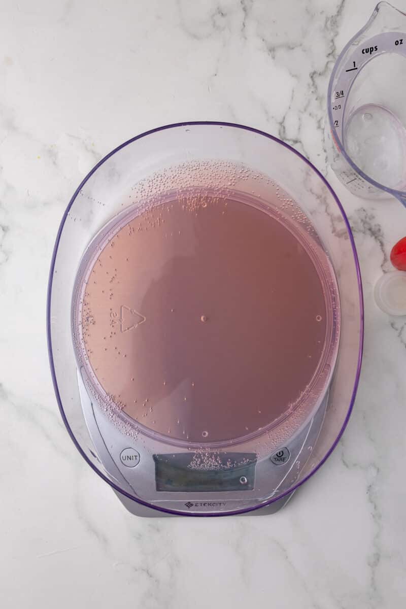 soda being measured on a scale with a wet measuring cup in the background on a white countertop