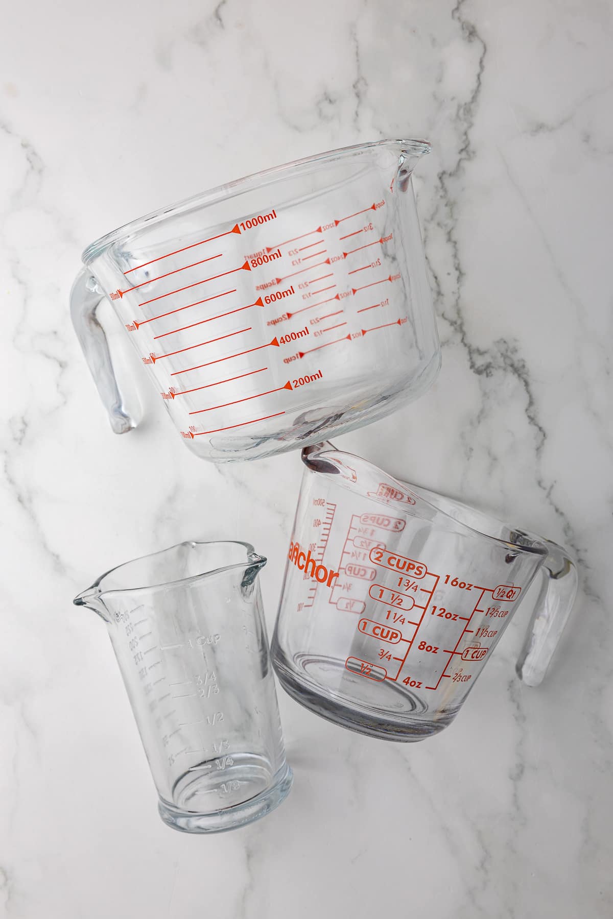 3 glass measuring cups used to measure wet ingredients in a recipe on a white countertop