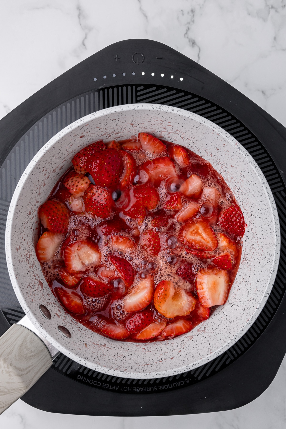saucepan with boiling strawberries and sugar on a hotplate