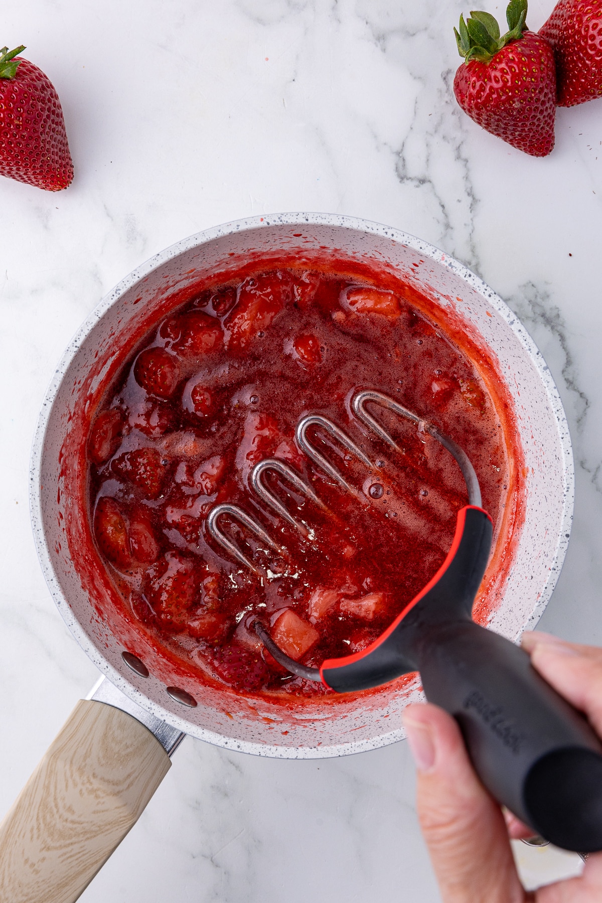 saucepan with strawberries and sugar on a hotplate with a potato masher