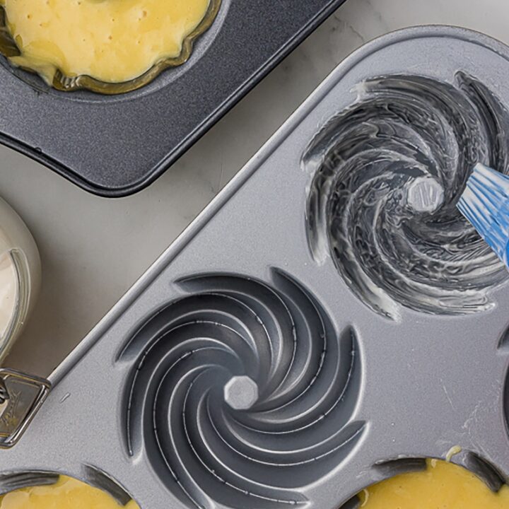 closeup of two mini bundt pans with a blue silicone brush and cake goop into the pans