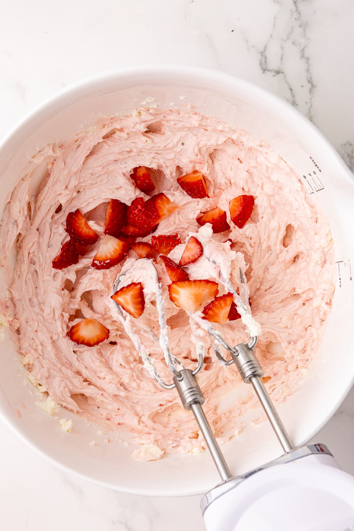 strawberry cream cheese in a white batter bowl with a kitchenaid hand mixer and fresh strawberry chunks