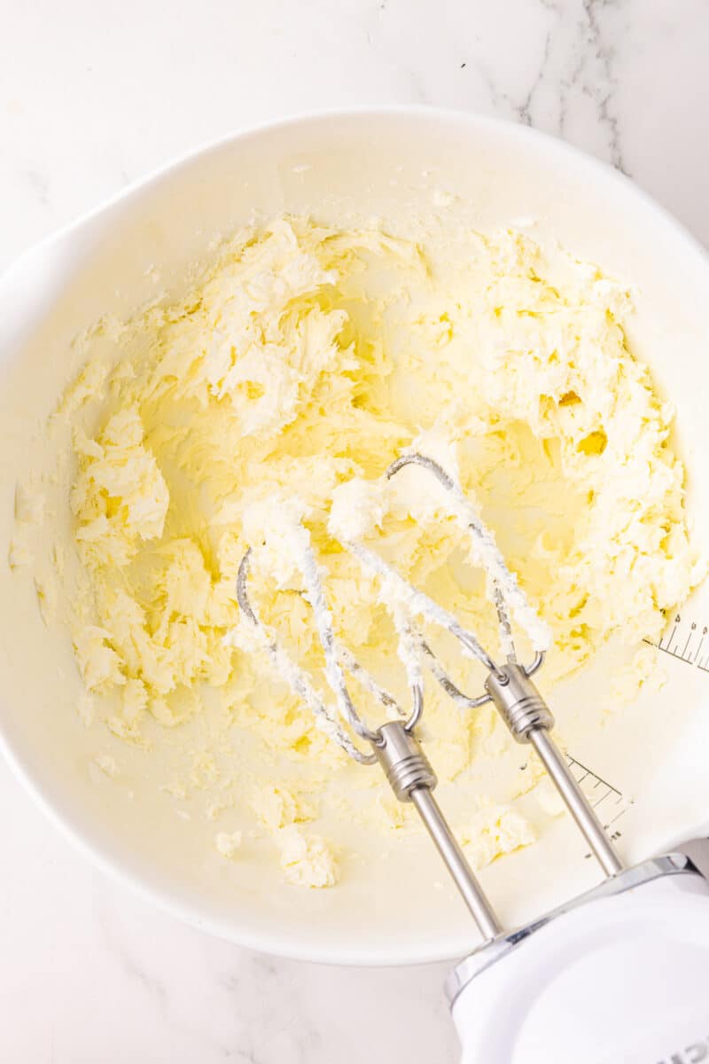 creamed cream cheese in a batter bowl with a cordless kitchenaid hand mixer