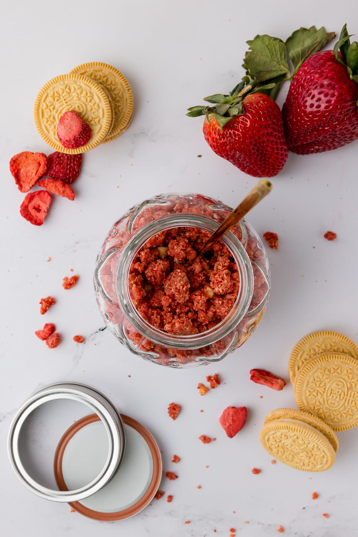 strawberry crunch in a glass jar with a golden spoon, fresh strawberries, golden oreos, and canning jar lid