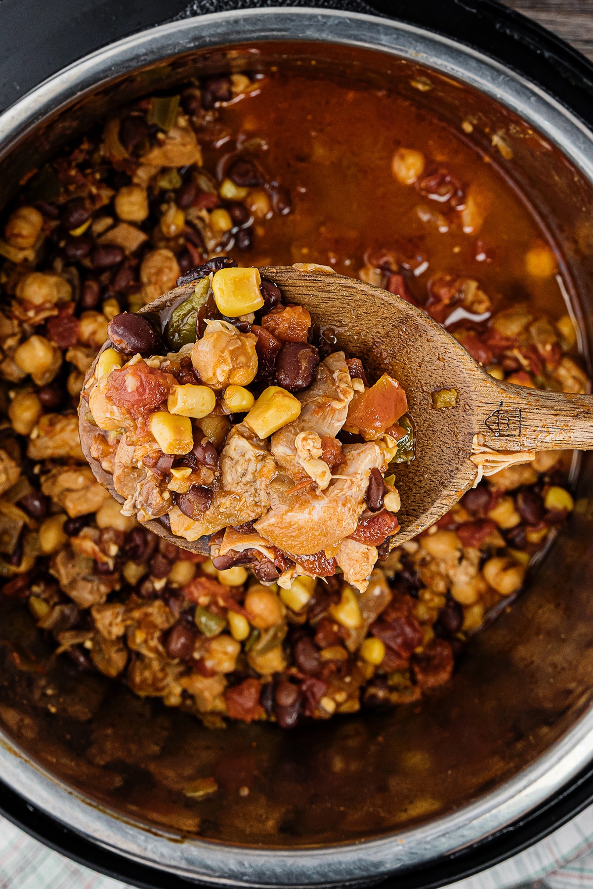 overhead photo of an instant pot of chicken chili on a wooden spoon