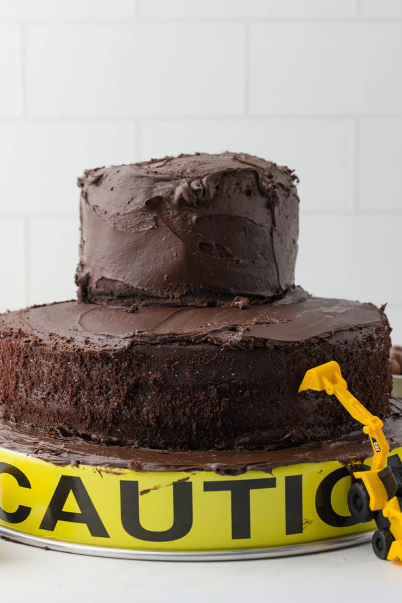 two tiered chocolate cake on a baking pan with a caution sign and a ini backhoe