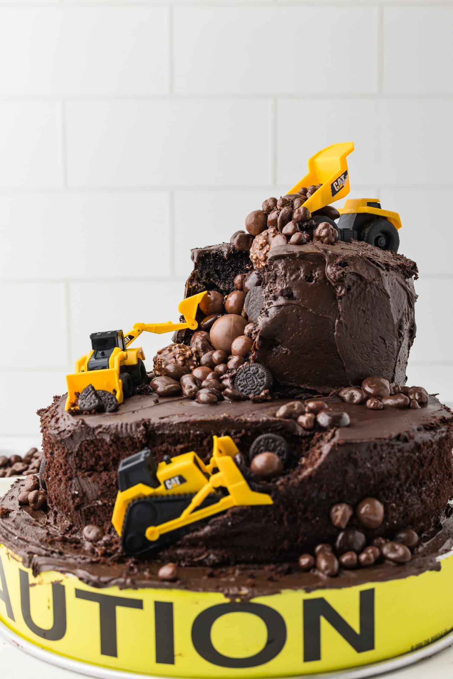 double tier chocolate cake with CAT construction toys and chocolate candy boulders on a white counter 
