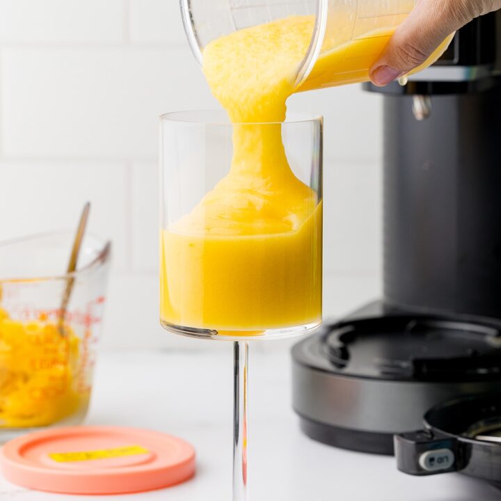 pouring the mango slushing into a clear goblet with the ninja creami in the background on a shite countertop