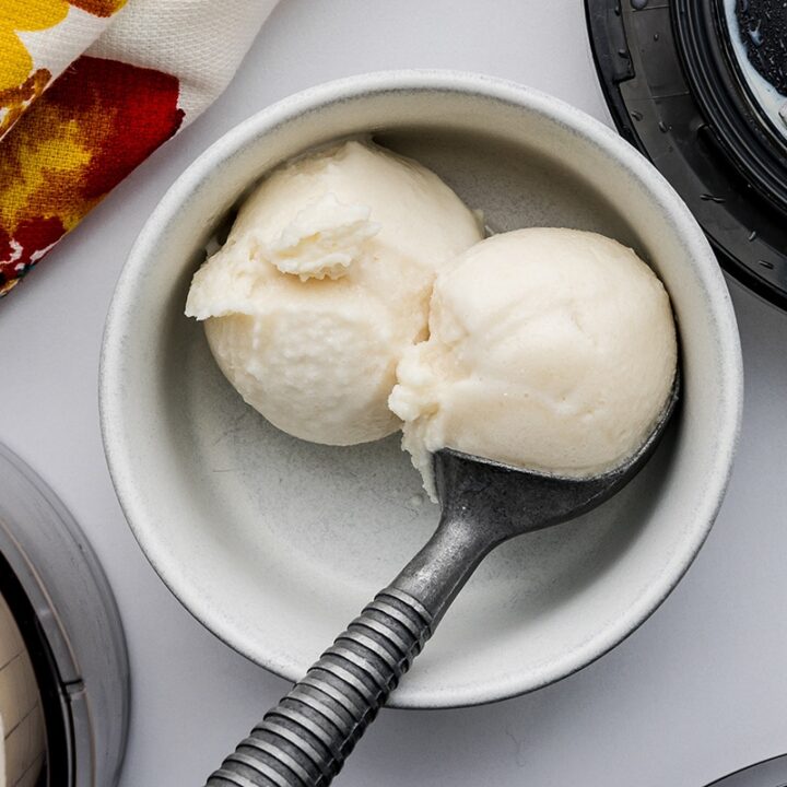 Two scoops of Ninja Vanilla protein ice cream in a small white bowl with a an ice cream scoop on a white countertop.