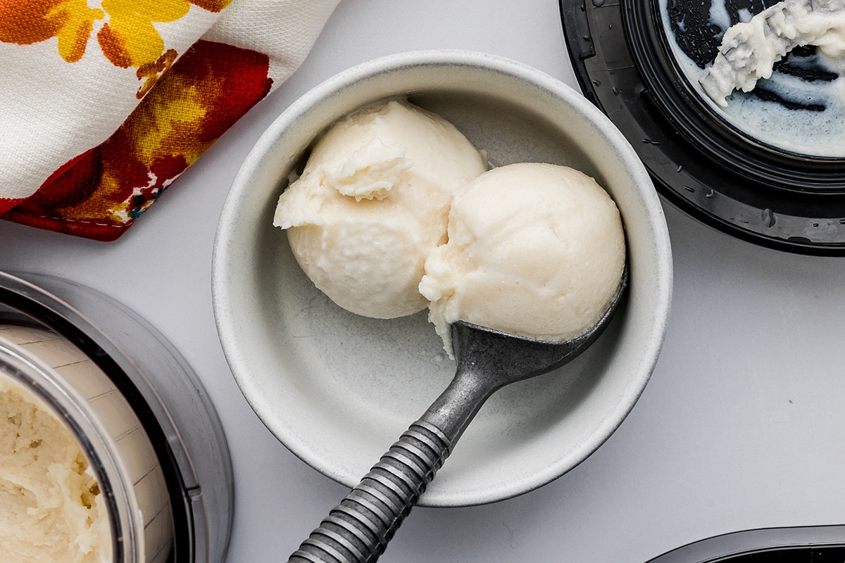 Two scoops of Ninja Vanilla protein ice cream in a small white bowl with a an ice cream scoop on a white countertop.