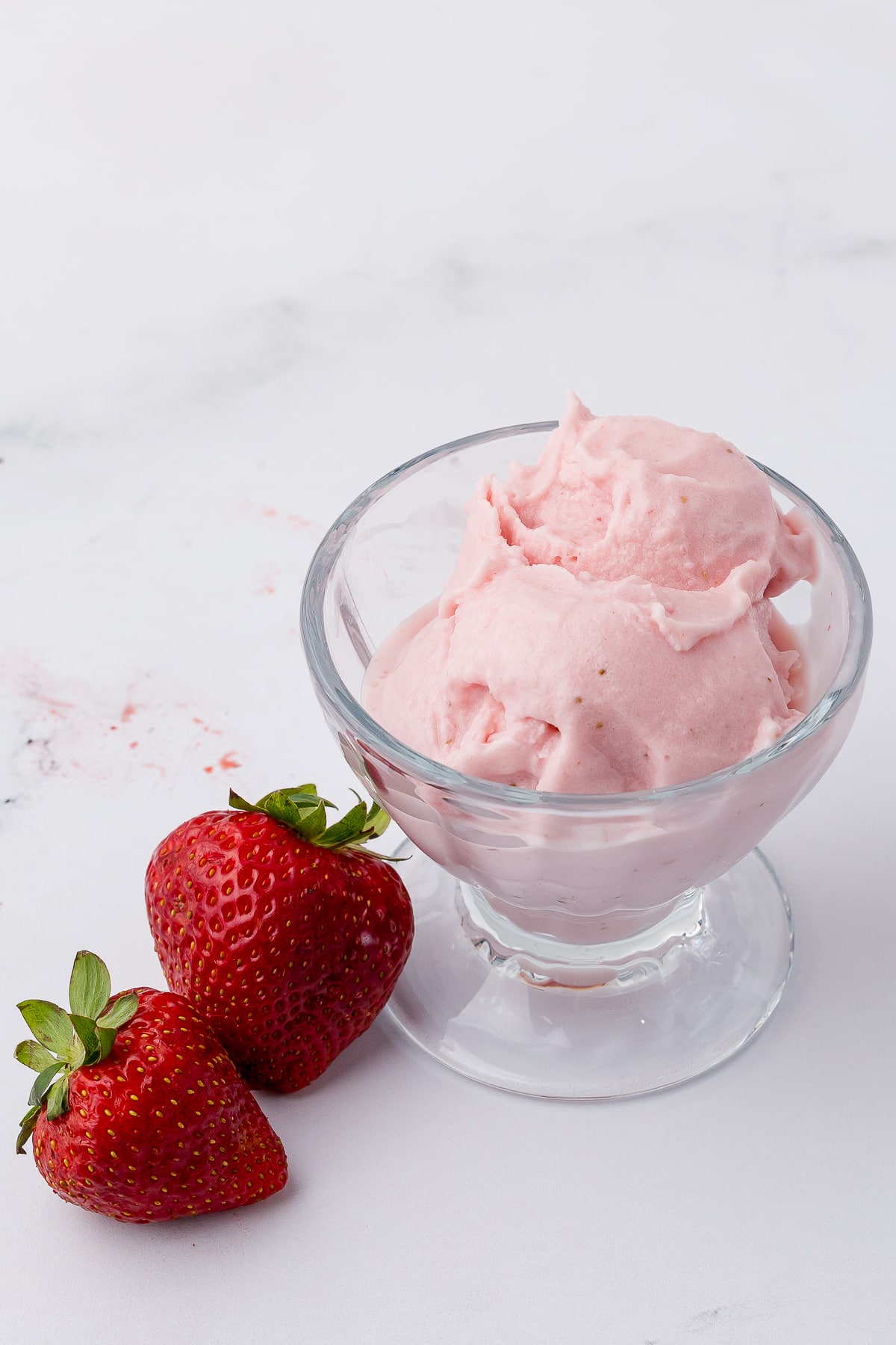 strawberry cheesecake ice cream in a sundae cup on a white counter with two fresh strawberries