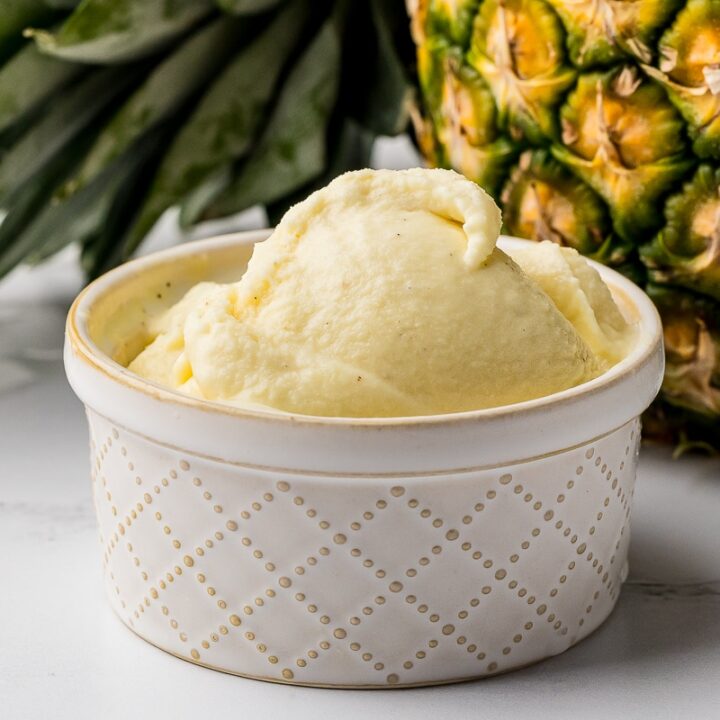 Bowl of homemade dole whip in a cream bowl with a pineapple in the background