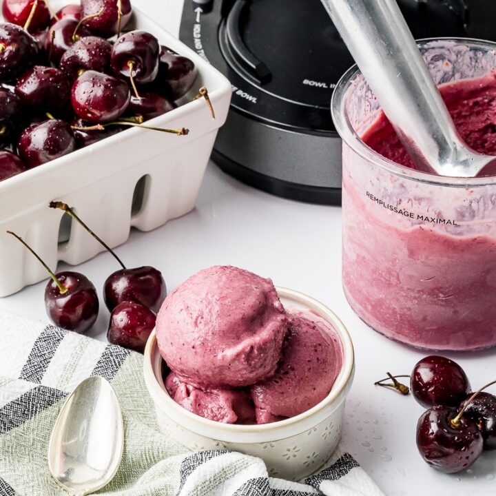 Ninja Creami Cherry Ice cream in a pint bowl with a berry bowl full of dark cherries and a bowl of ice cream on a white counter