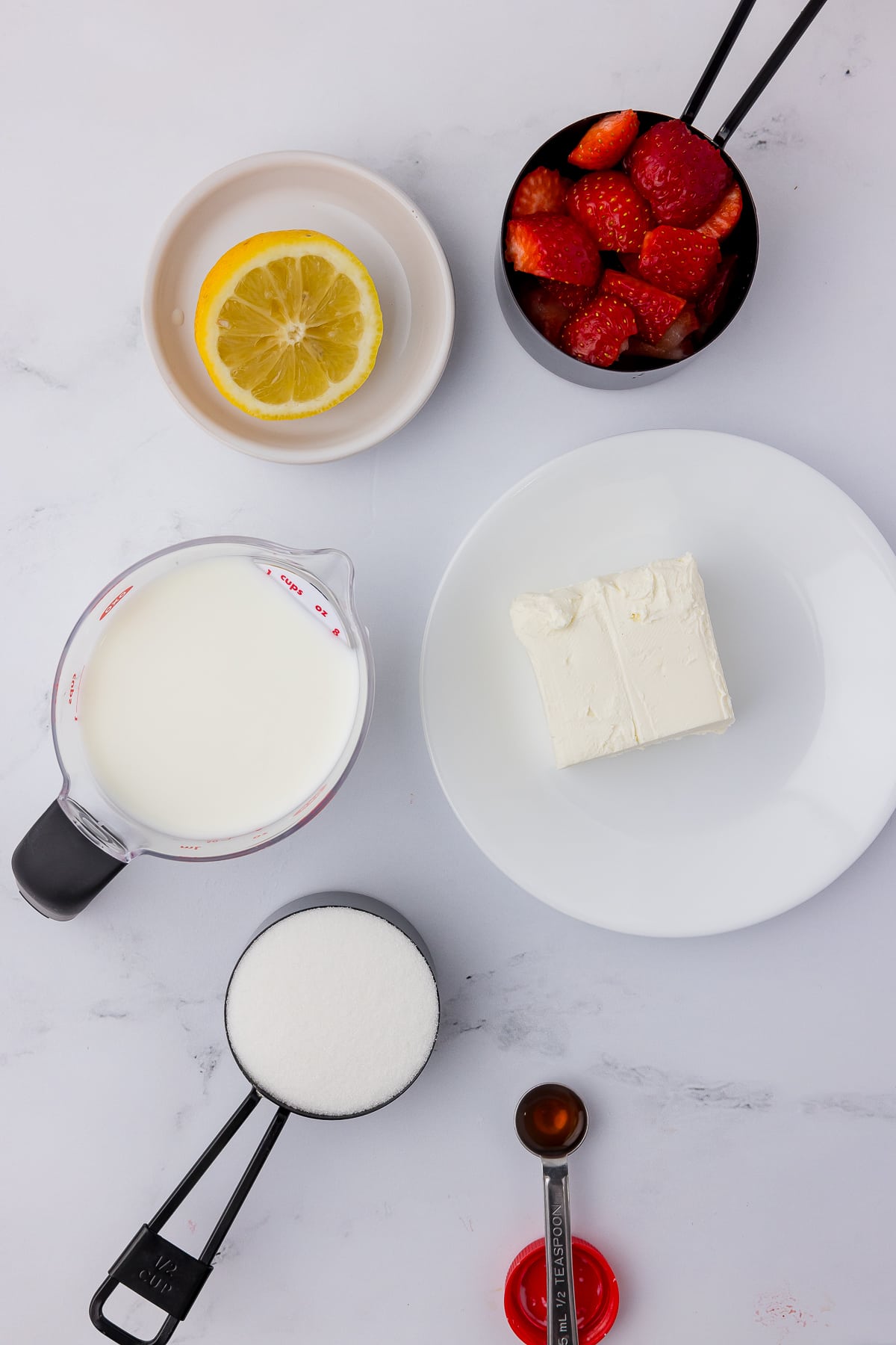 ingredients for ninja creami strawberry cheesecake ice cream including strawberries, lemon, cream cheese, milk, sugar, and vanilla