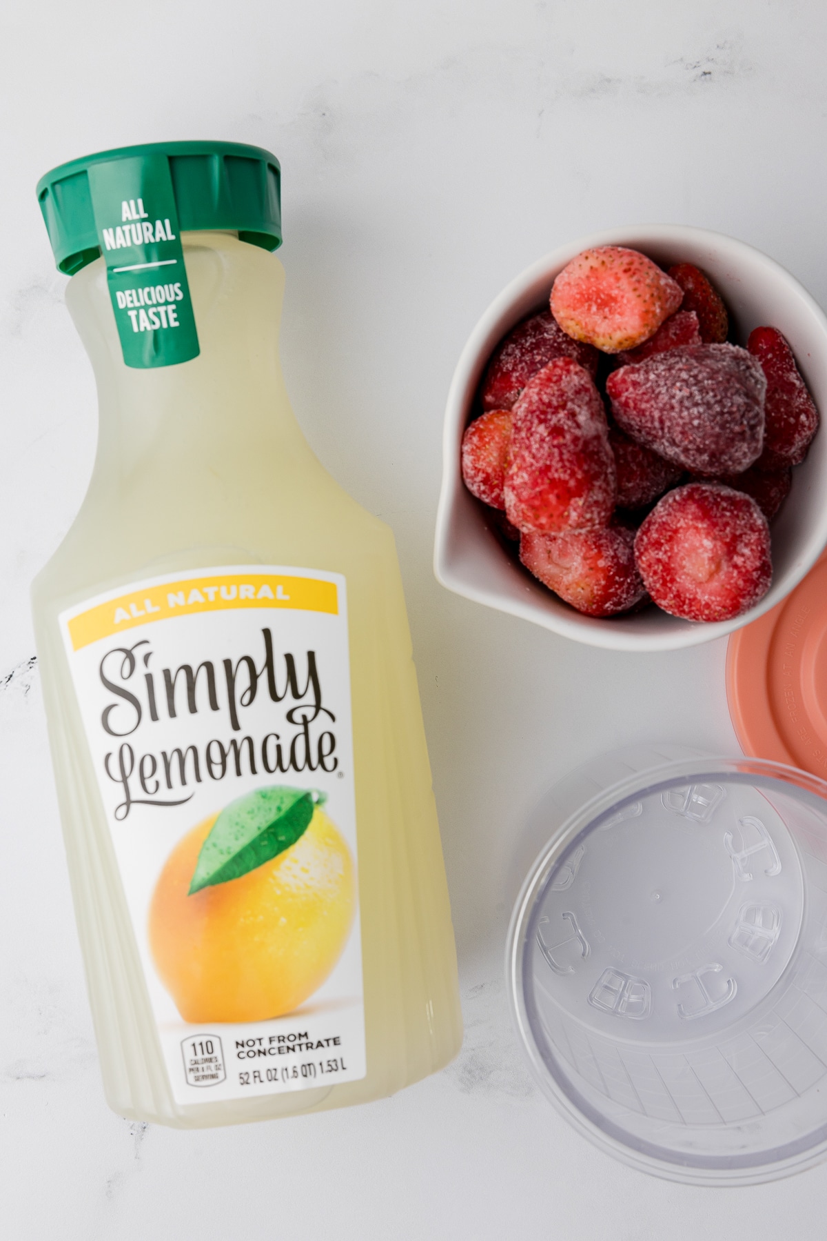 simply lemonade, frozen strawberries in a cup and a ninja creami pint jar on a white counter