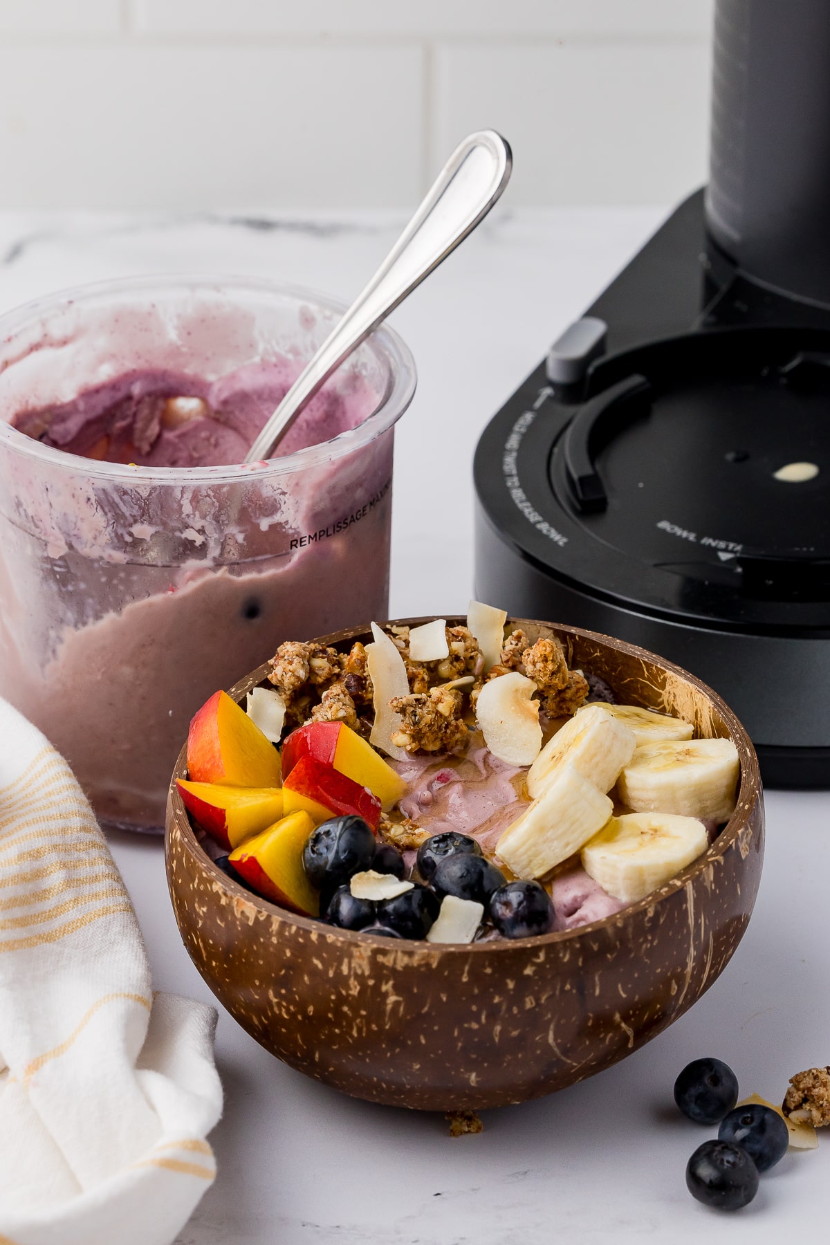 acai bowl with fresh fruit on a white countertop, nectarine, blueberries, bananas, and a ninja creami with granola