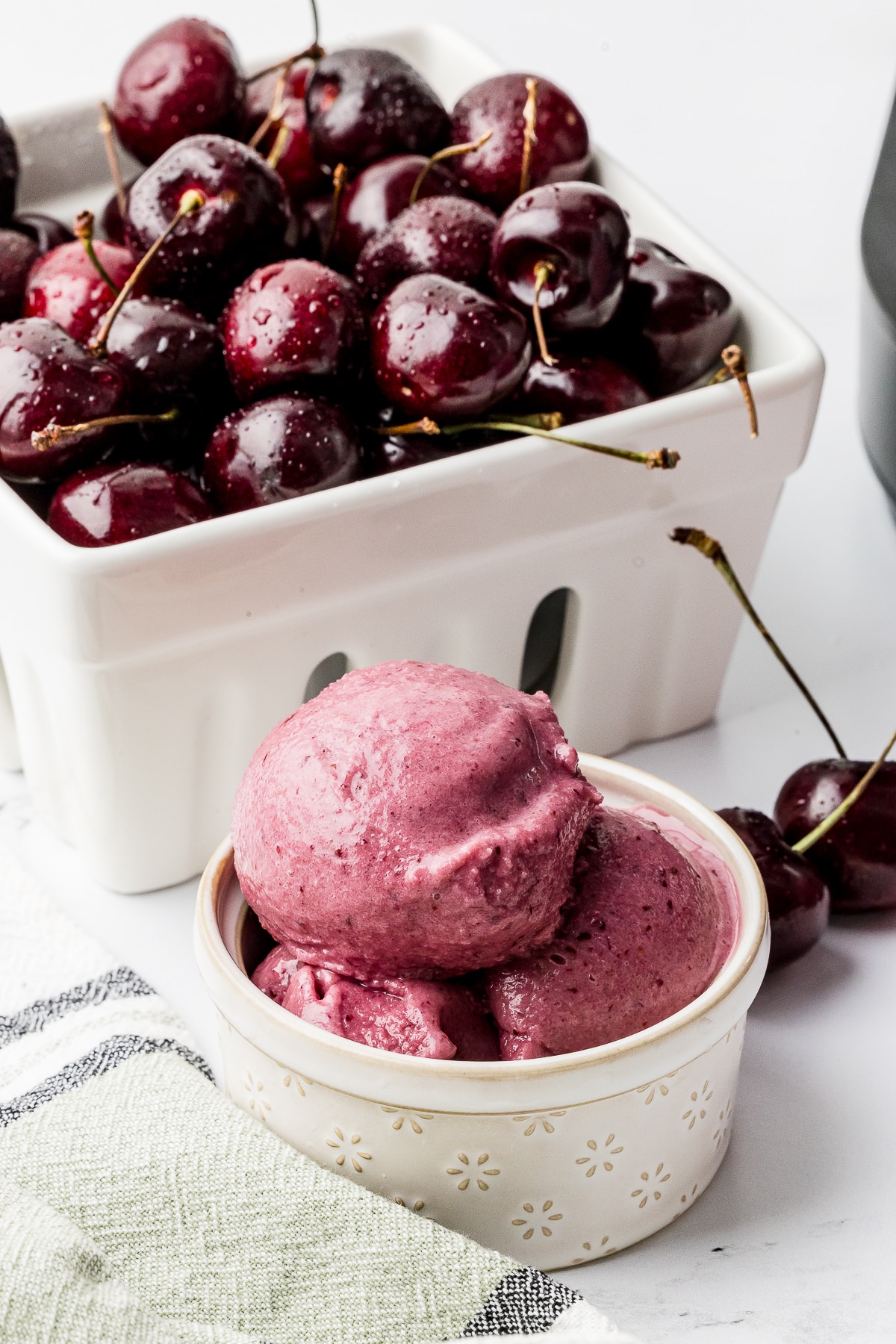 Ninja Creami Cherry Ice cream in a pint bowl with a berry bowl full of dark cherries and a bowl of ice cream on a white counter