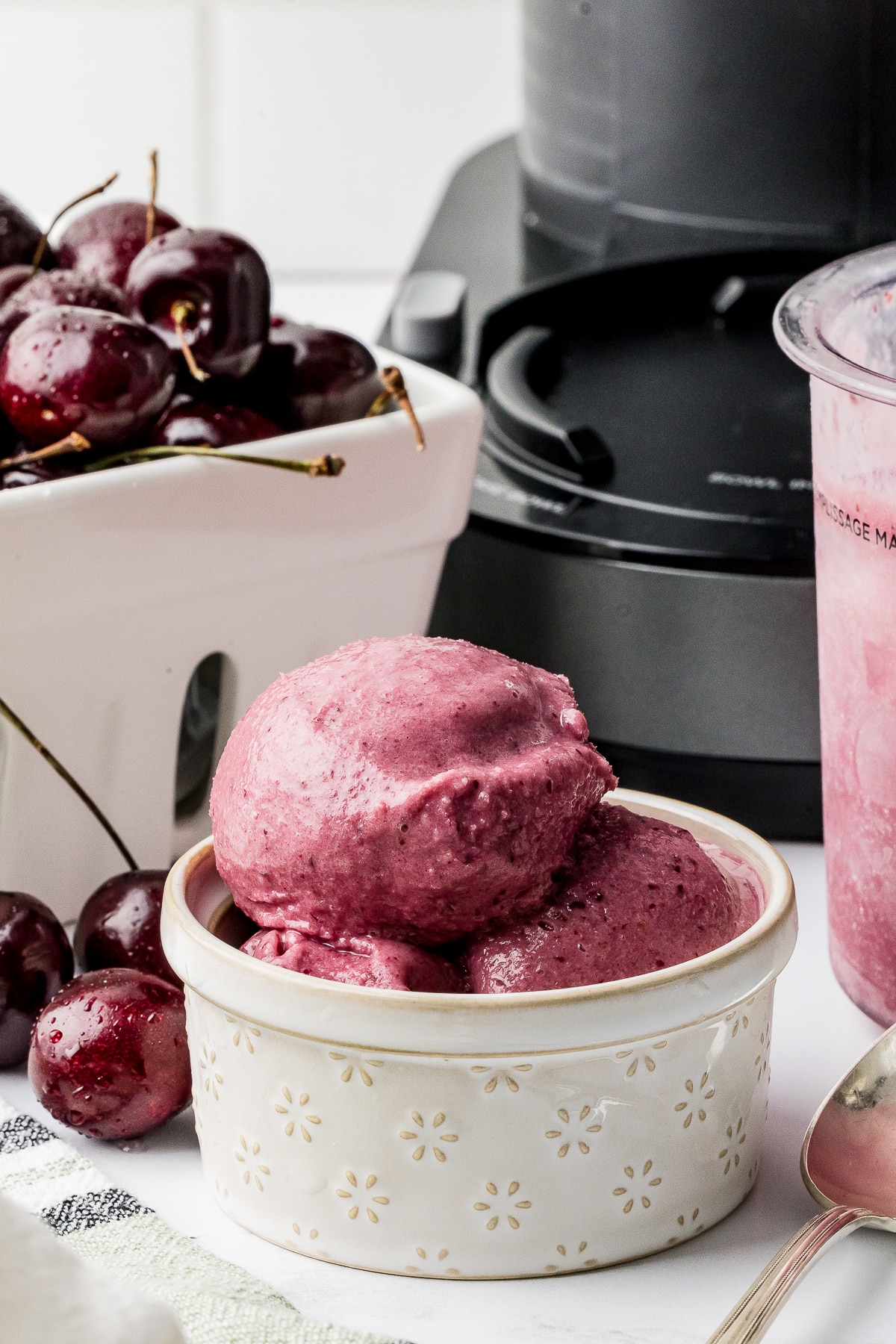 Ninja Creami Cherry Ice cream in a pint bowl with a berry bowl full of dark cherries and a bowl of ice cream on a white counter