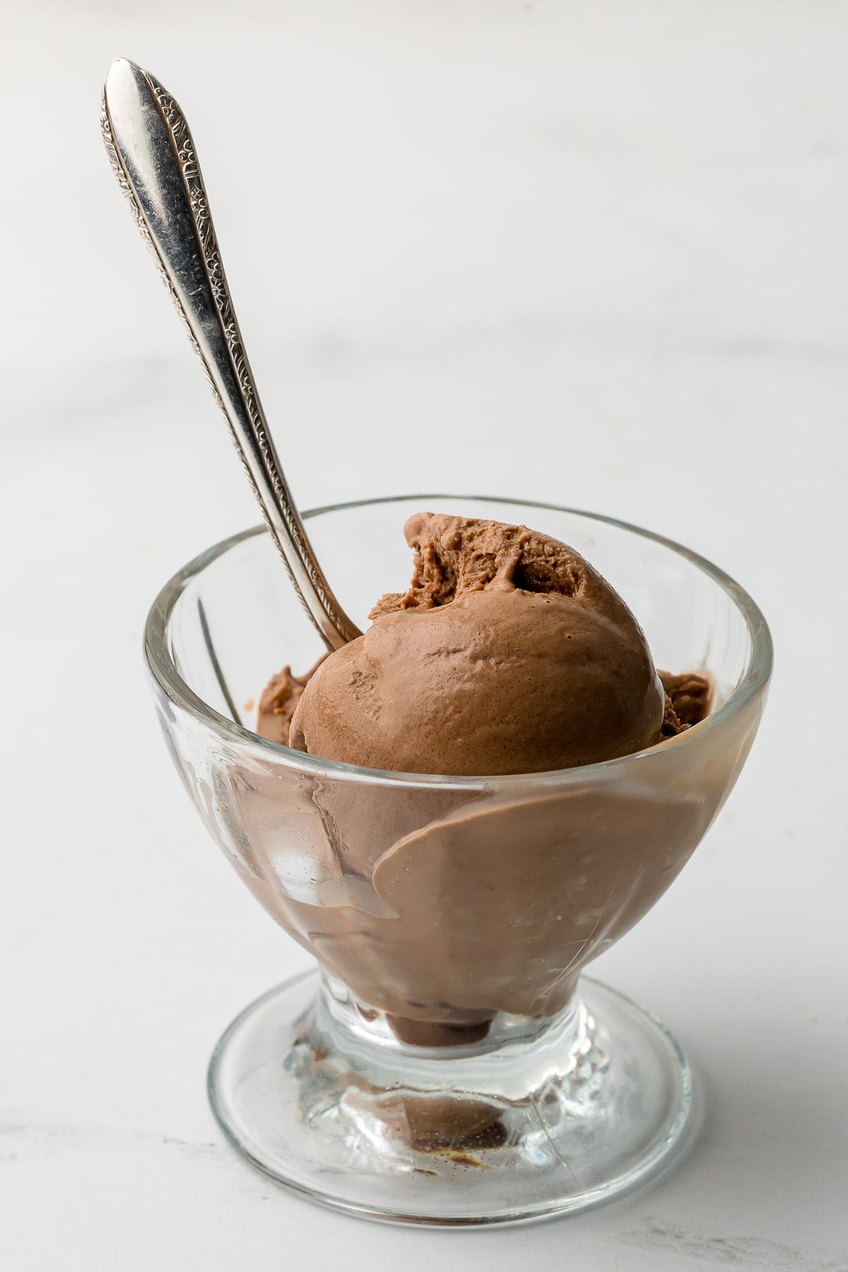 once scoop of chocolate ice cream in a sundae bowl with a silver spoon