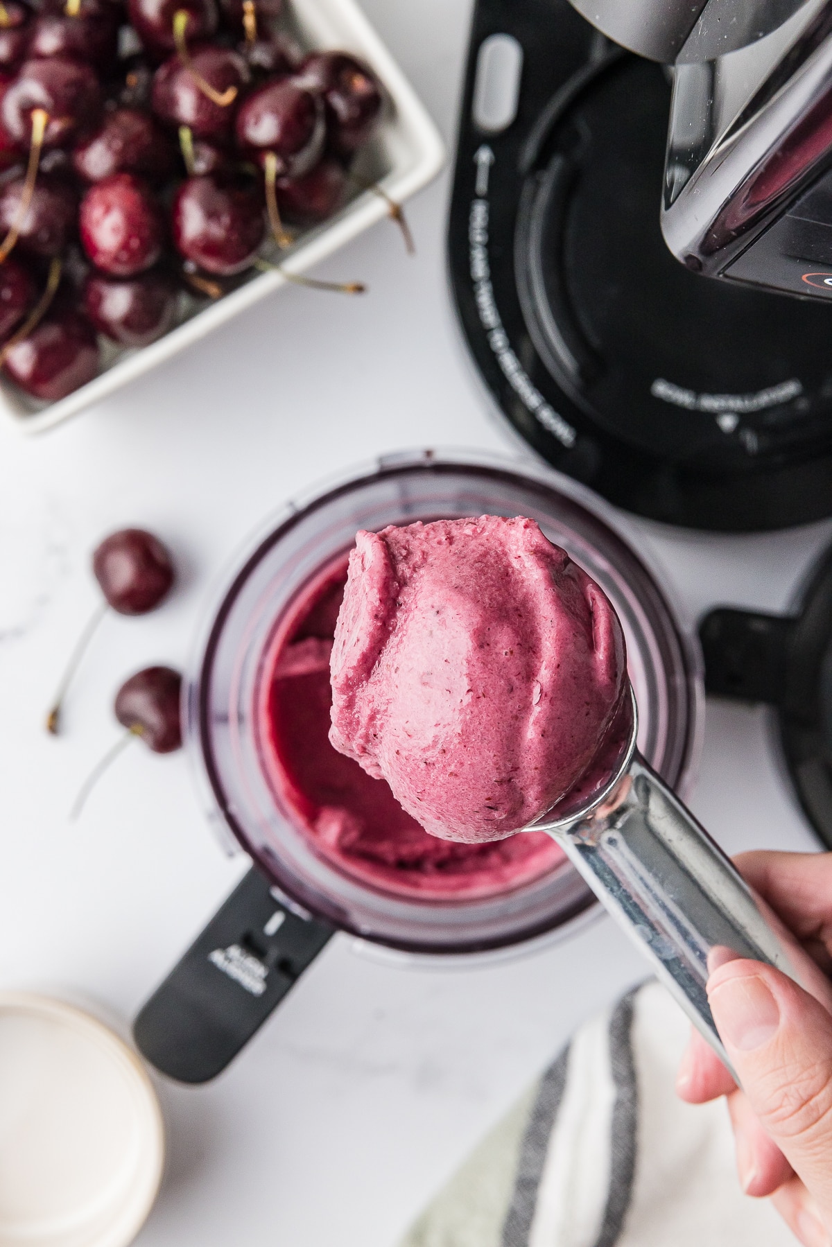 Ninja Creami Cherry Ice cream in a pint bowl with a berry bowl full of dark cherries and a bowl of ice cream on a white counter