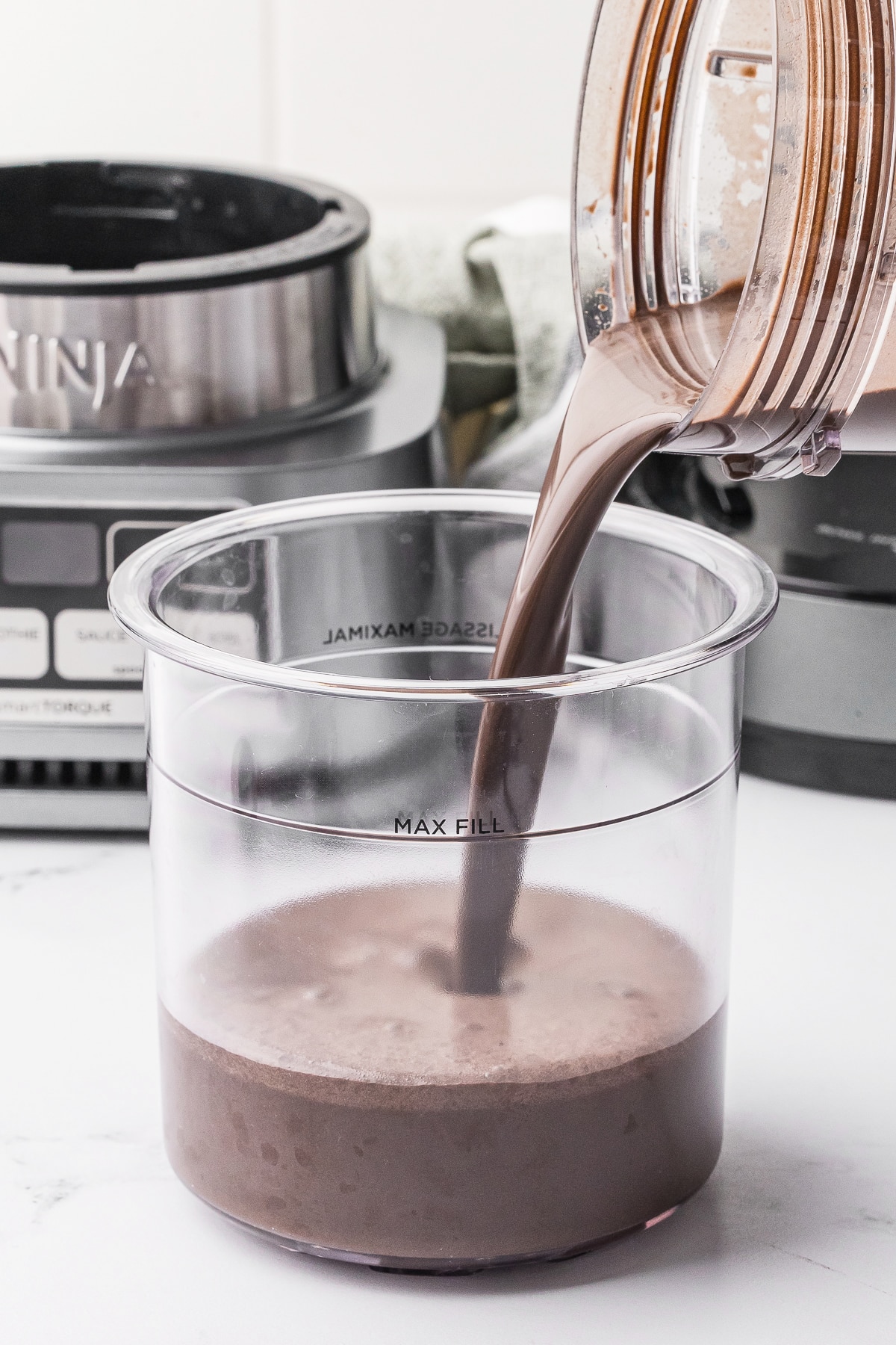 ninja creami pint jar with chocolate ice cream mixture being poured in