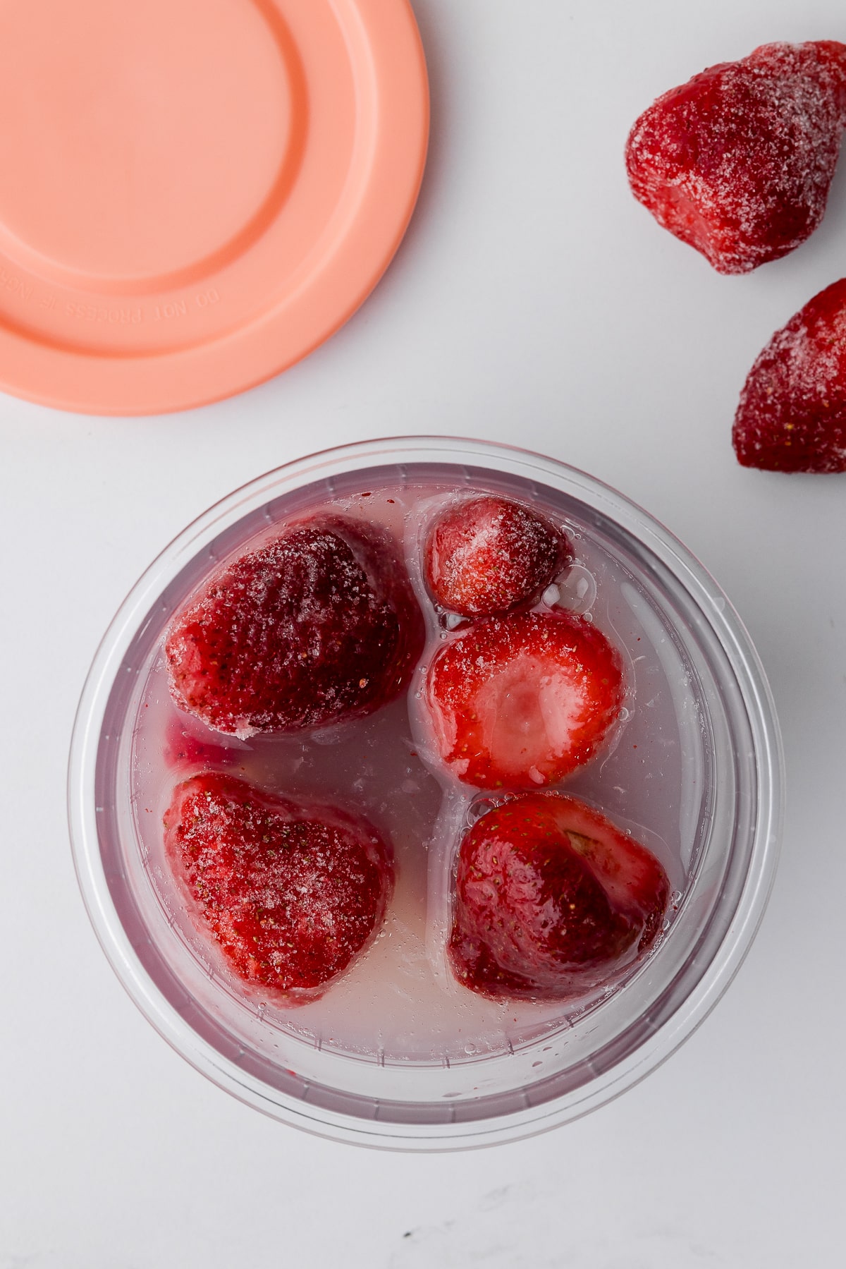 strawberries in a ninja creami pint jar with lemonade to the fill line and a peach colored cover on a white counter