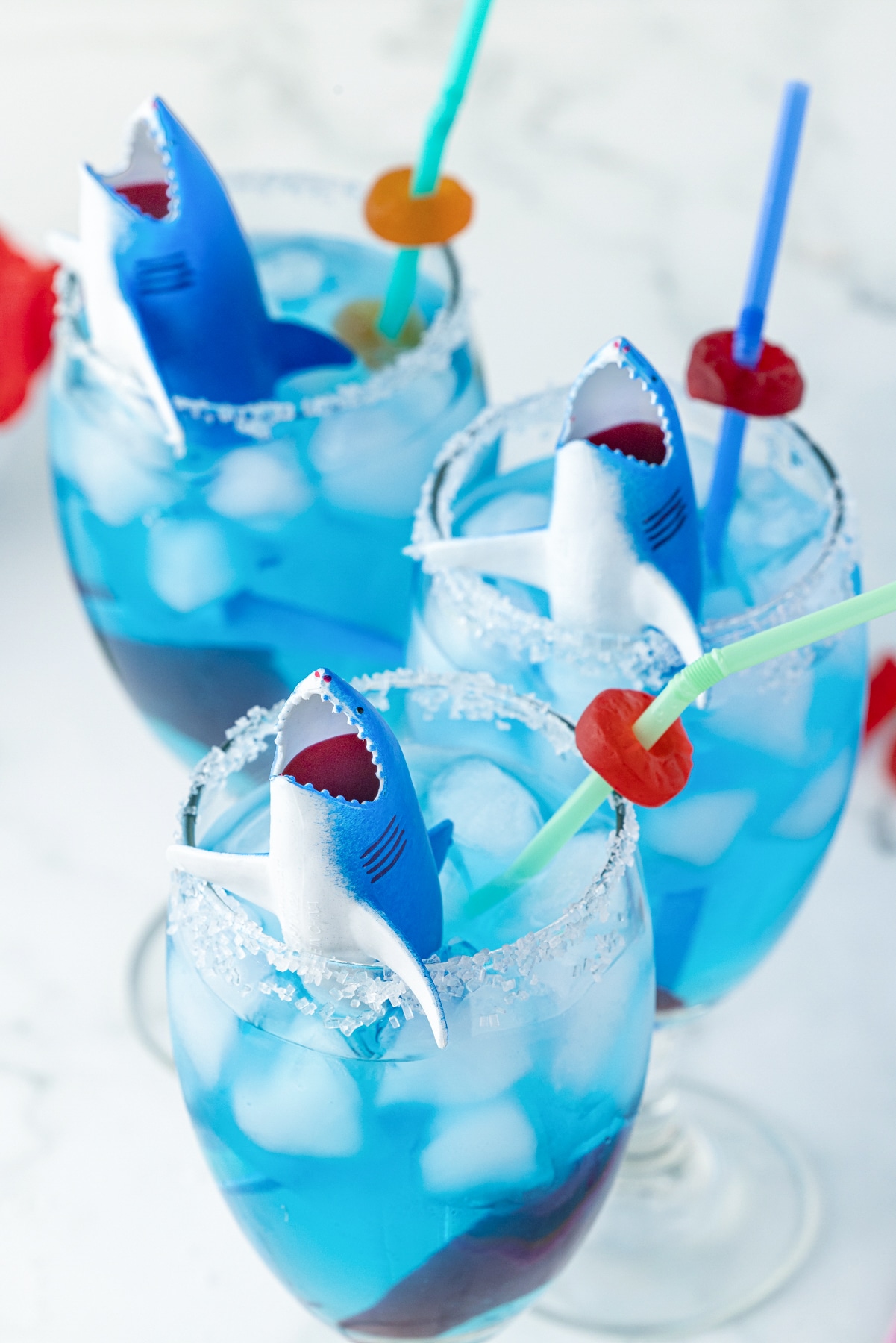 three sharks peeking up from a glass that is rimmed with wilton sanding sugar, and has ice with blue gatorade