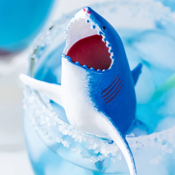 Plastic shark toy filled with grenadine in a cup filled with blue gatorade and ice