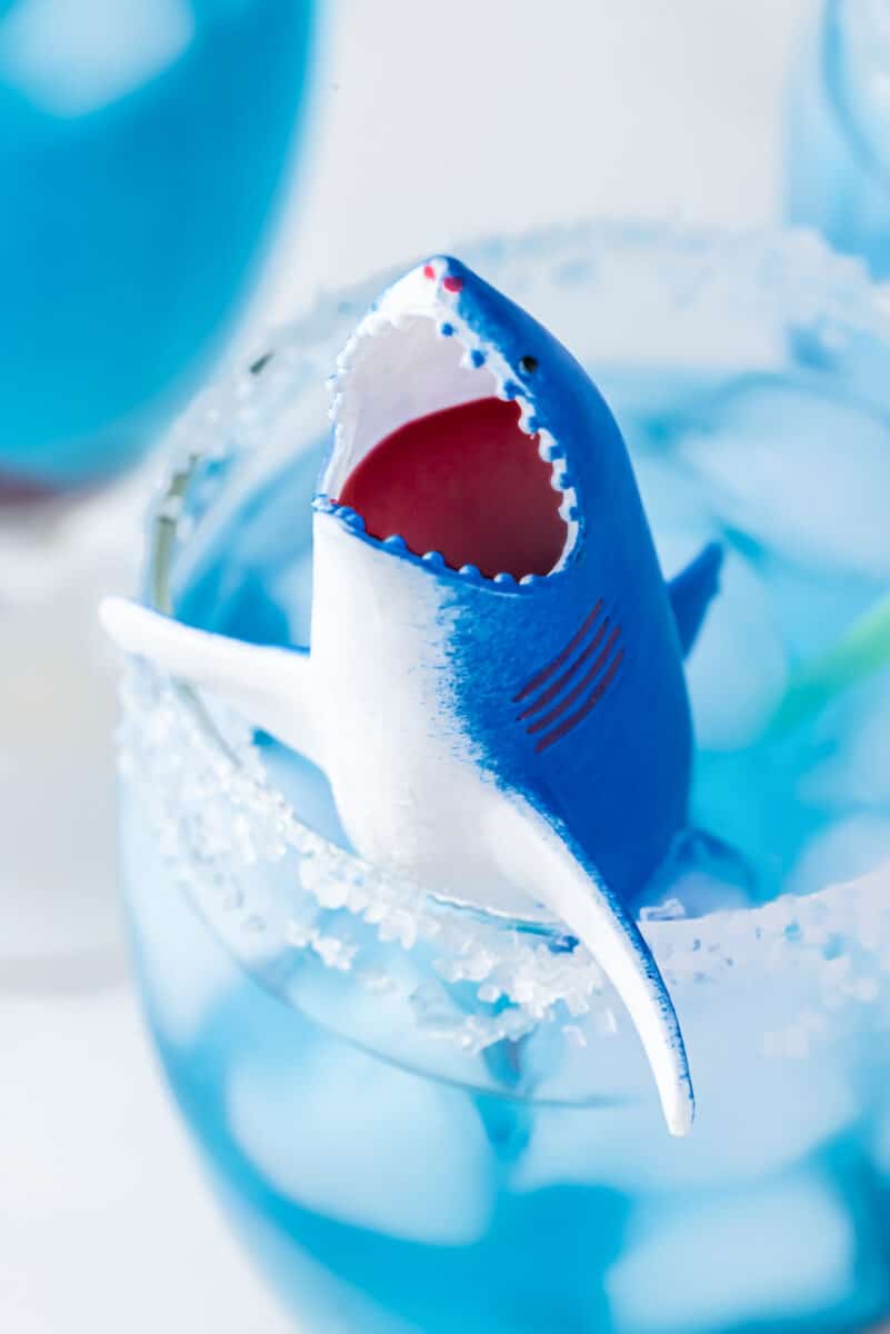 Plastic shark toy filled with grenadine in a cup filled with blue gatorade and ice