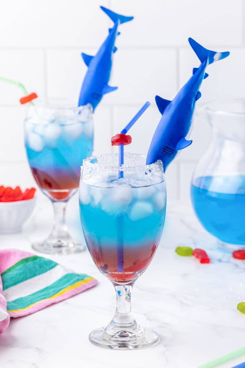 Plastic shark toy biting onto a glass filld with blue gatorade and grenadine