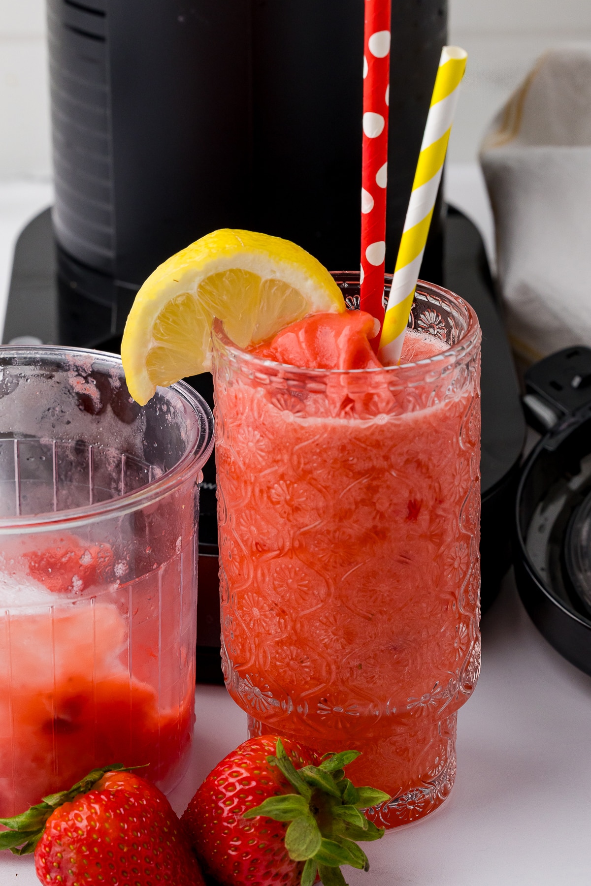 close up of glass with strawberry lemonade slusie, a lemon wedge, and two straws