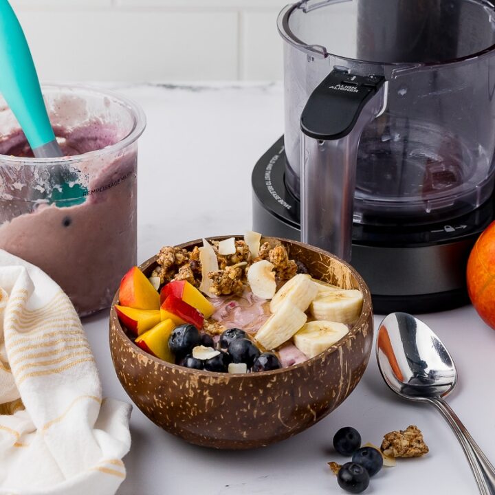 Acai bowl on a white countertop with the ninja creami in the background, with a nectarine.