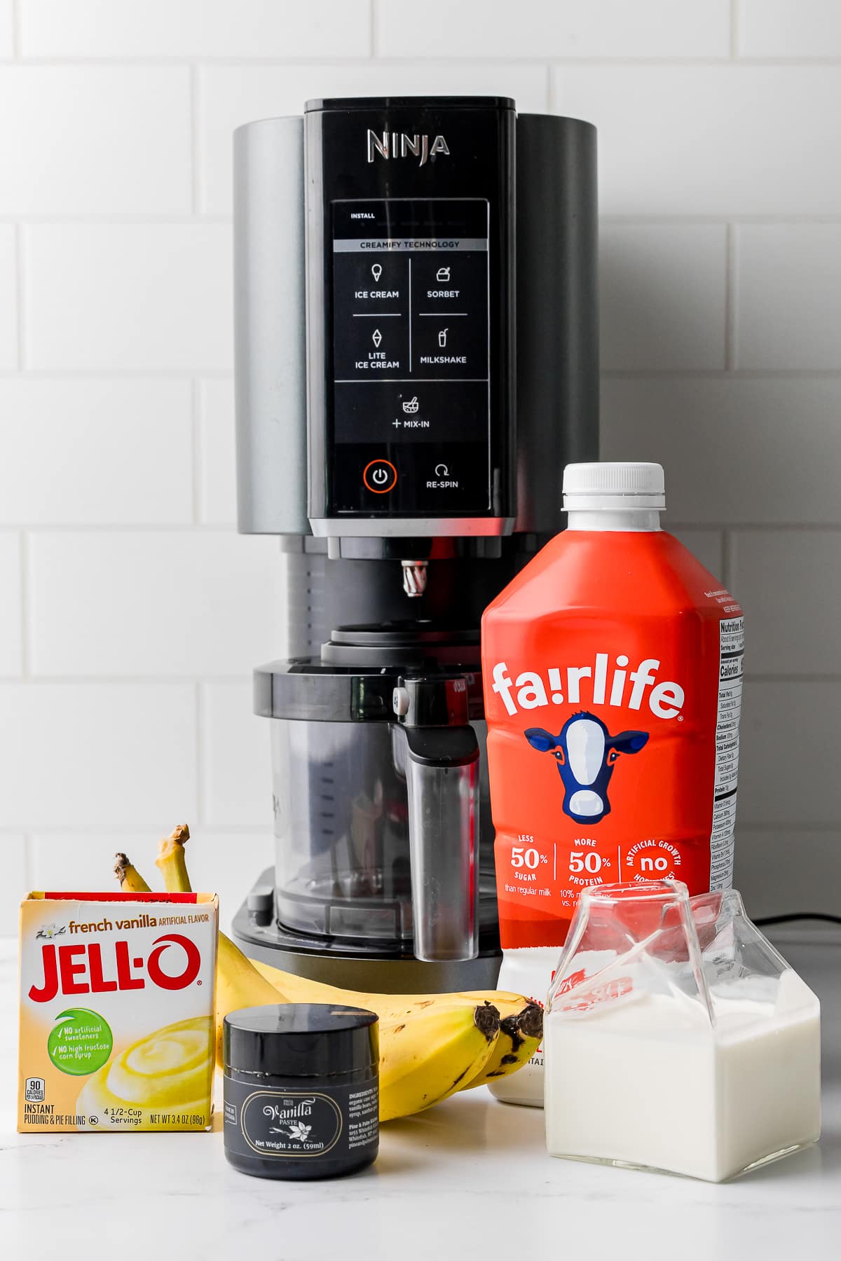 Ninja Creami machine on the counter with ingredients: Jell-o, bananas, milk and vanilla