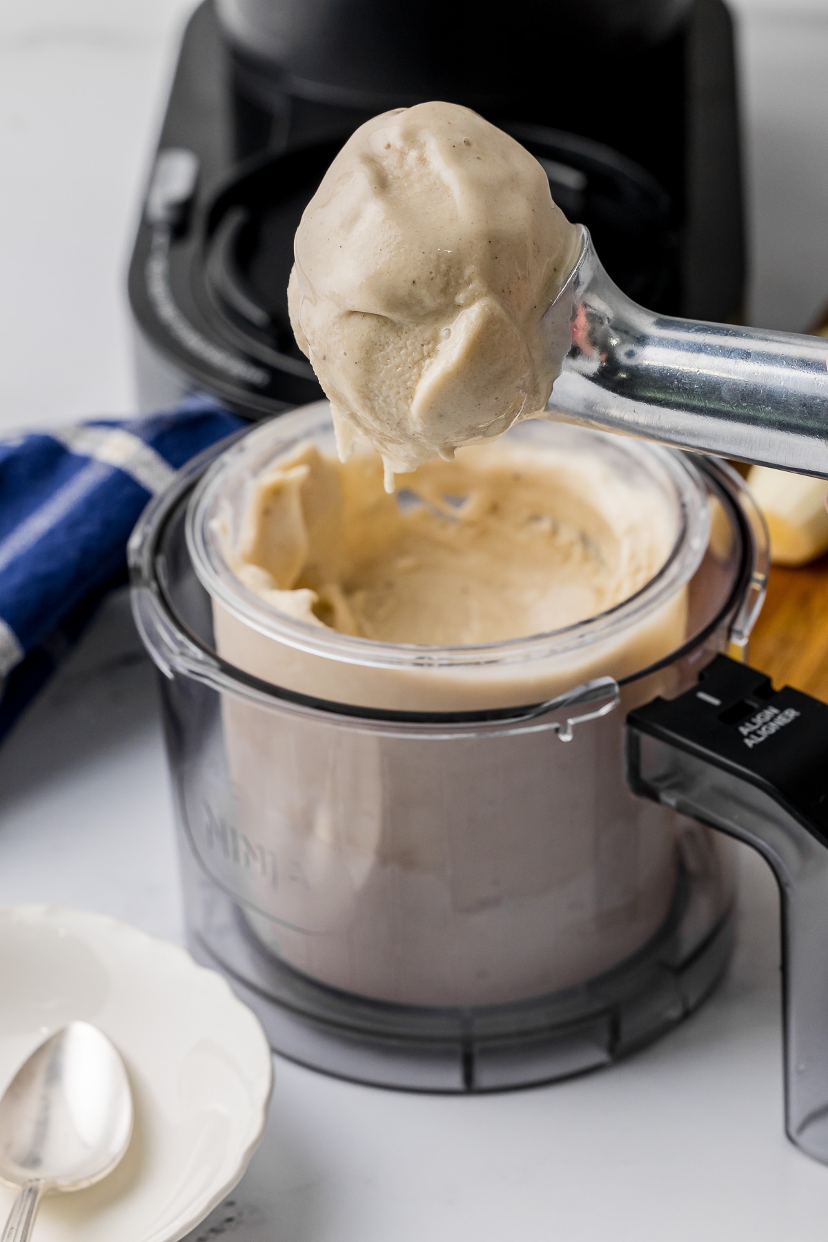 Silver ice cream scoop full of banana ice cream coming out of a Ninja Creami container