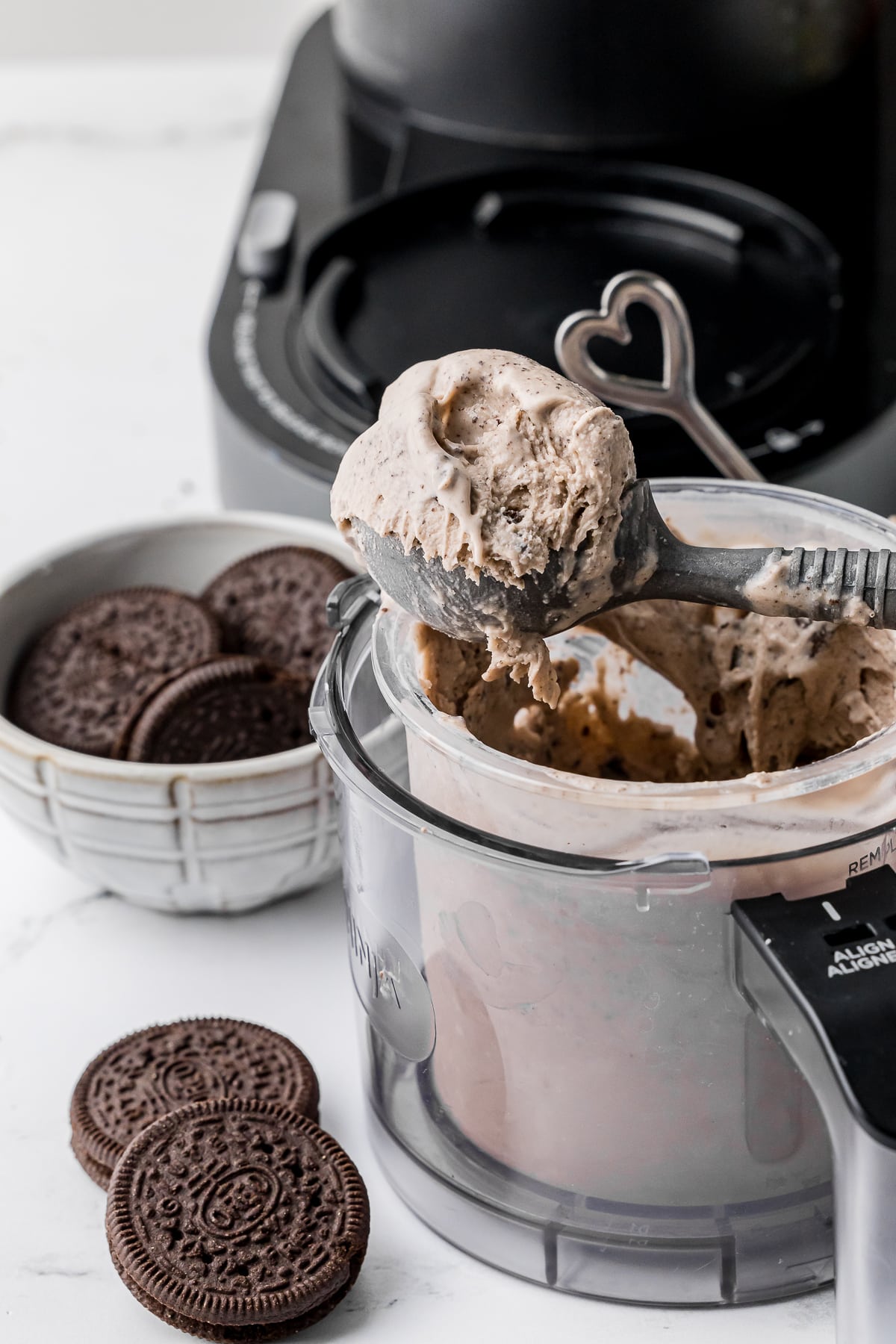 cookies and cream ice crem in a ninja creami pint jar with an ice cream scoop and oreo cookies