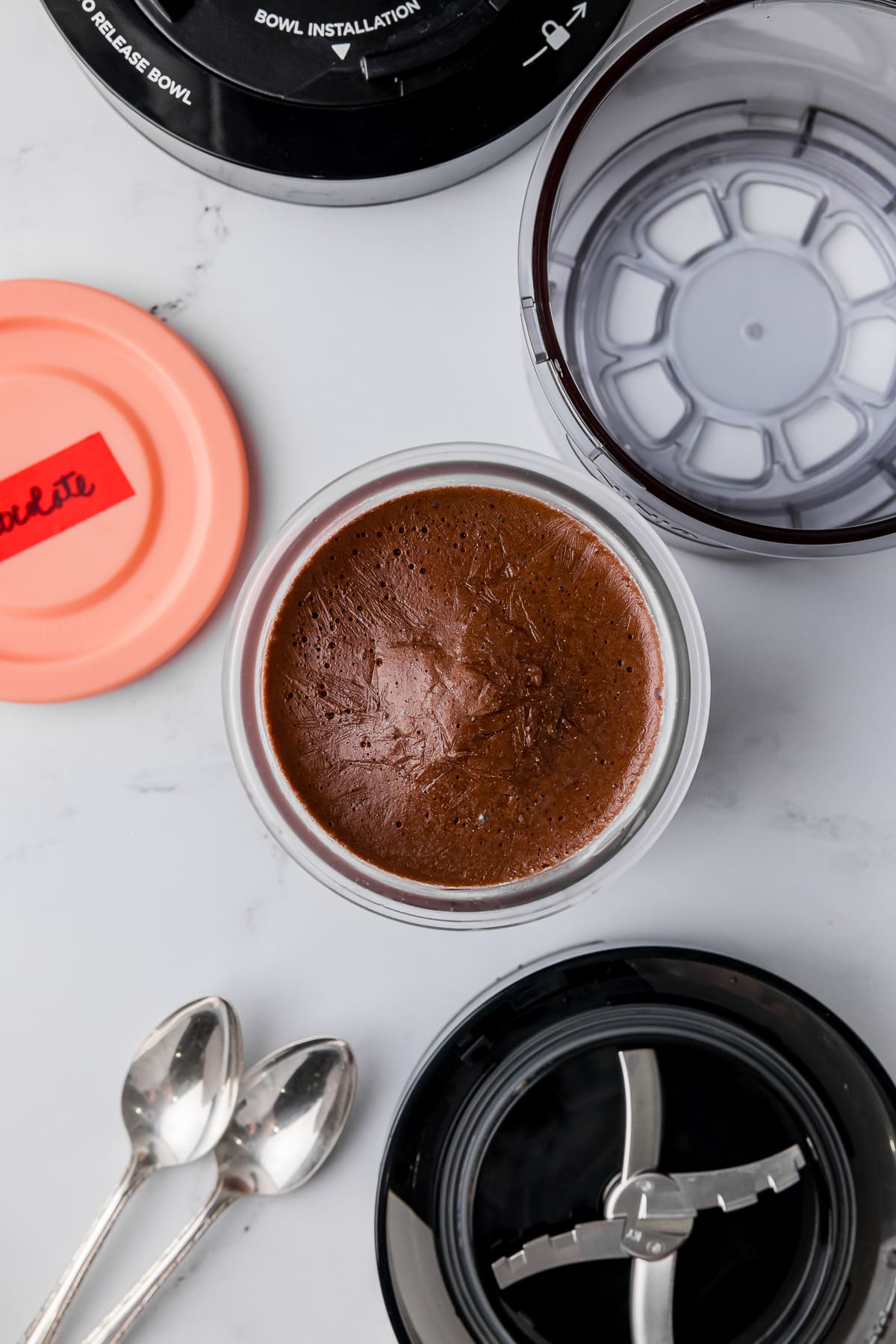 frozen chocolate ice cream in a ninja creami pint jar with two spoons, blades and the exterior bowl