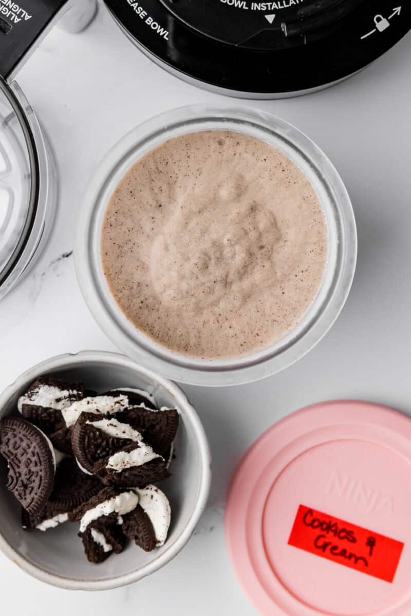 frozen cookies and cream ice cream in a ninja creami pint jar with oreos in bowl