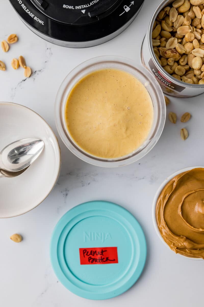 frozen peanut butter ice cream in a ninja creami pint jar with creamy peanut butter, a ninja lid, a bowl with a spoon and a jar of peanuts