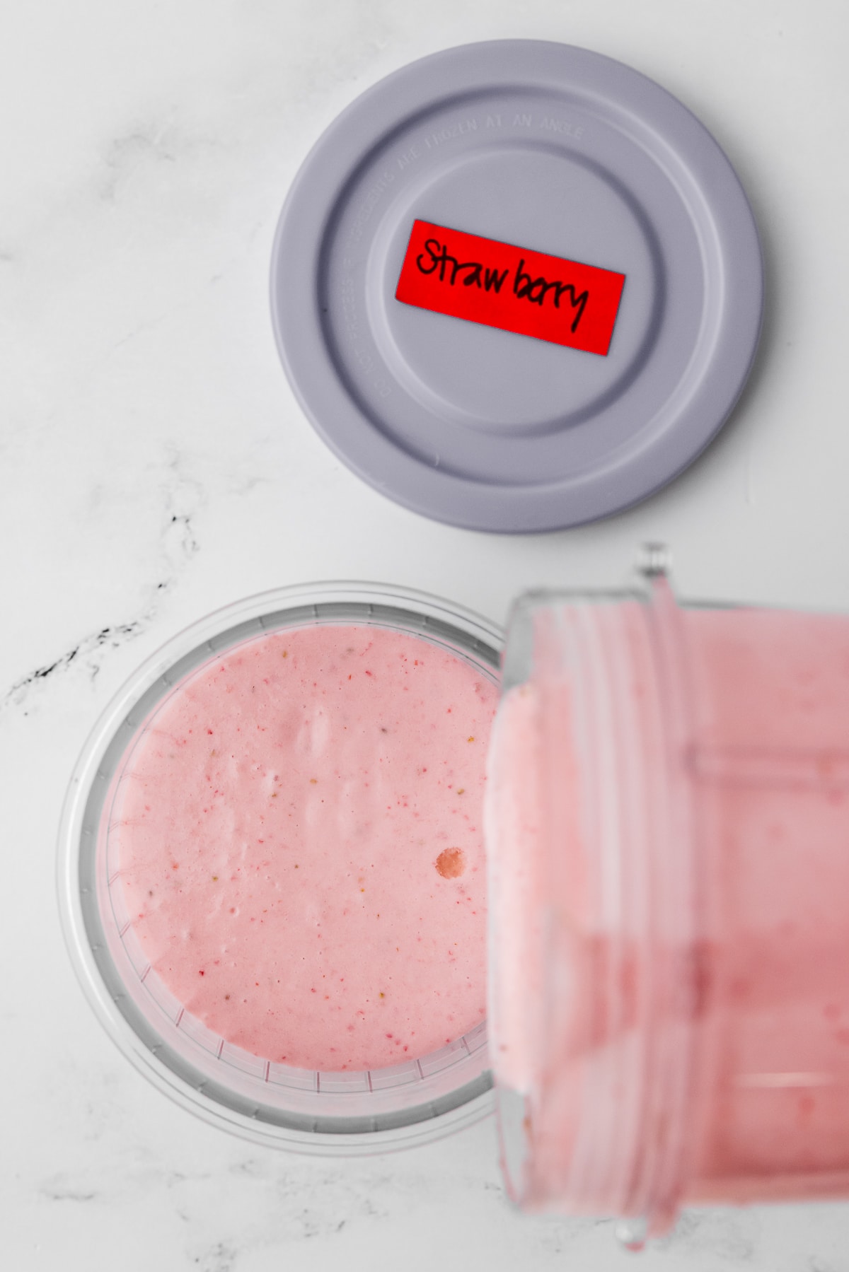 pouring liquid strawberry ice cream mixture into a pint jar with a grey lid, "strawberry" written on red masking tape