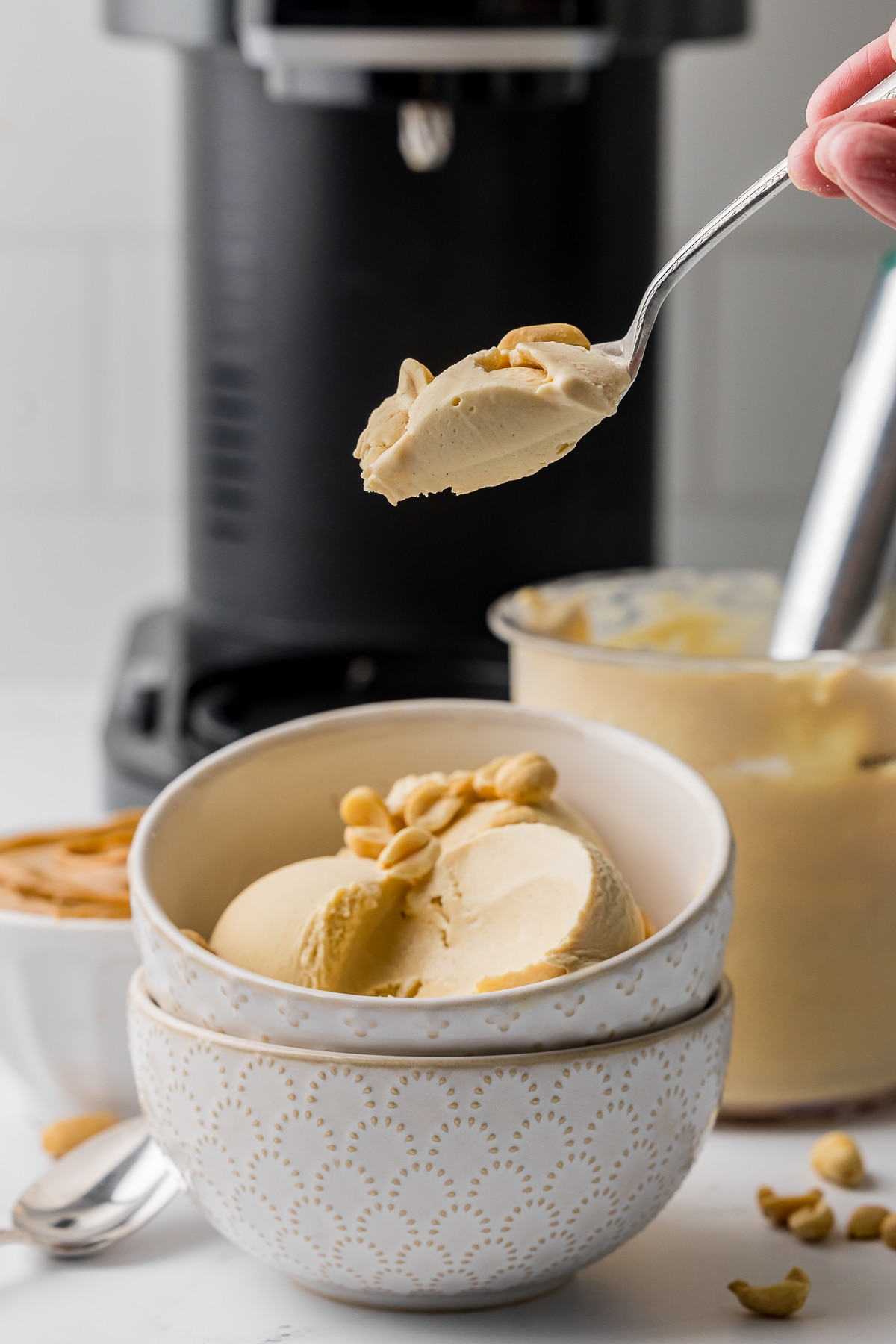 peanut butter ice cream in a beige ice cream bowl with a spoon full of ice cream in front of a ninja creami ice cream machine