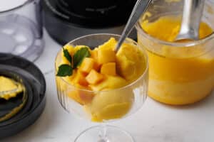 closeup of mango sorbet in a champagne flute with chunks of mango and mint leaves