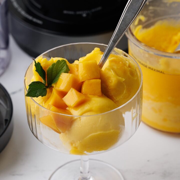 closeup of mango sorbet in a champagne flute with chunks of mango and mint leaves