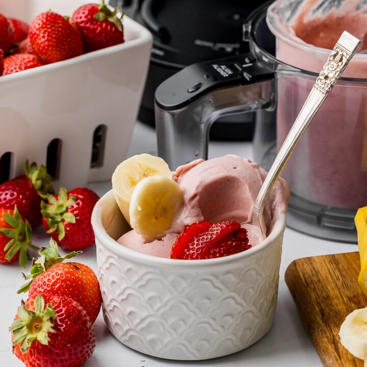 bowl of strawberry banana ice cream with sliced bananas and sliced strawberries with a ninja creami pint jar and a berry bowl full of strawberries