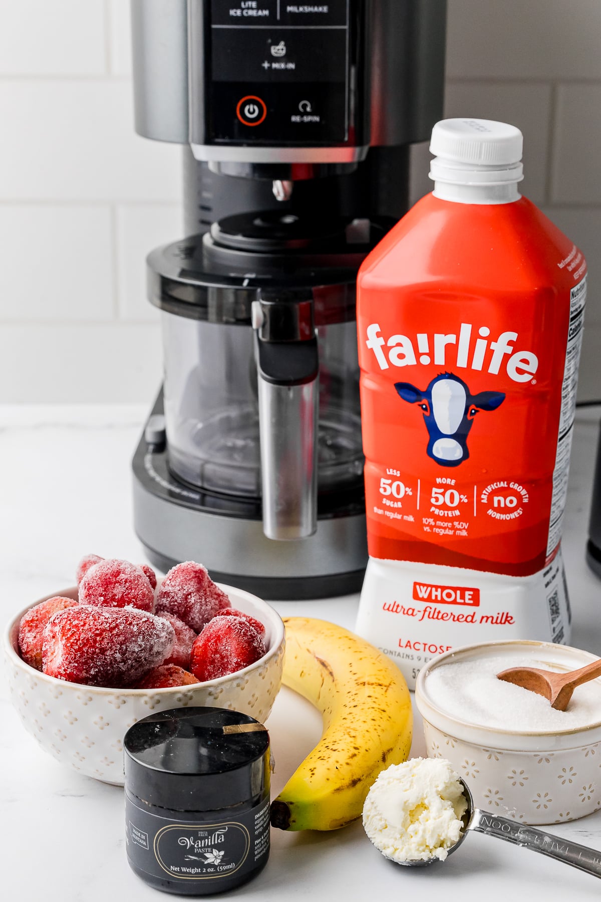 ingredients for strawberry banana ice cream including fairlife whole milk, a banana, frozen strawberries, vanilla paste, cream cheese, and sugar