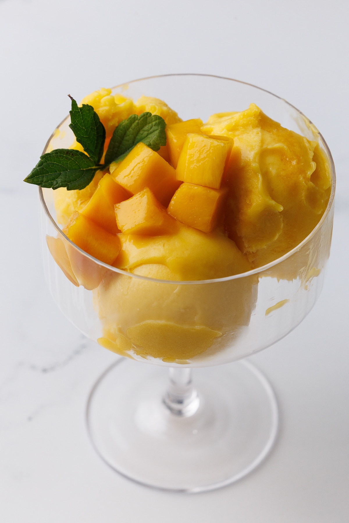 champagne glass filled with mango sorbet and chunks of mango with mint leaves